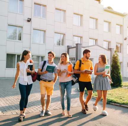 Five friendly students are walking after they passed test outside the college building and discuss the project Free time of a students, bachelor`s campus life rhythm. Five friendly students are walking after they passed test outside the college building and discuss the project, smiling, enjoying, carefree