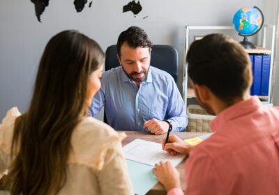 Tourists buying a trip abroad with a travel agent You got a deal. Young man signing a sales contract for a holiday vacation with his wife. Sales representative closing a deal for a timeshare sale with some customers at the travel agency