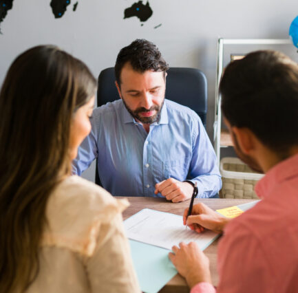 Tourists buying a trip abroad with a travel agent You got a deal. Young man signing a sales contract for a holiday vacation with his wife. Sales representative closing a deal for a timeshare sale with some customers at the travel agency